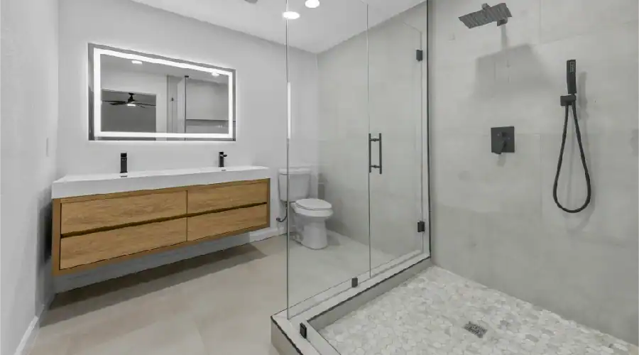 Modern bathroom remodel in Bedford, TX featuring glass shower, tile flooring, floating vanity, and frameless mirror with LED.