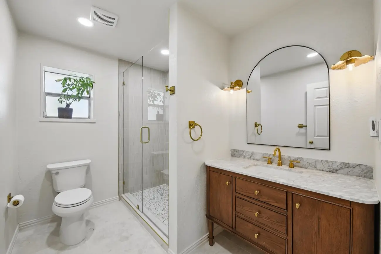 Primary bathroom — arched mirror, wood vanity & glass shower · Colleyville